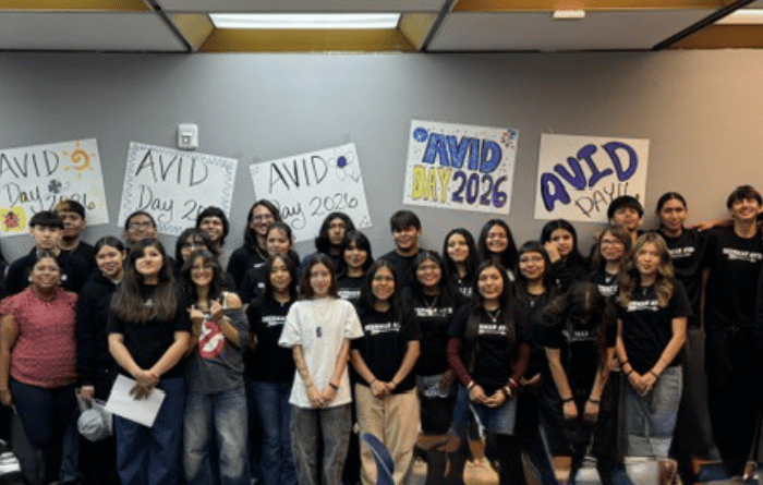 A group of students and staff pose together in front of posters celebrating AVID Day 2026.