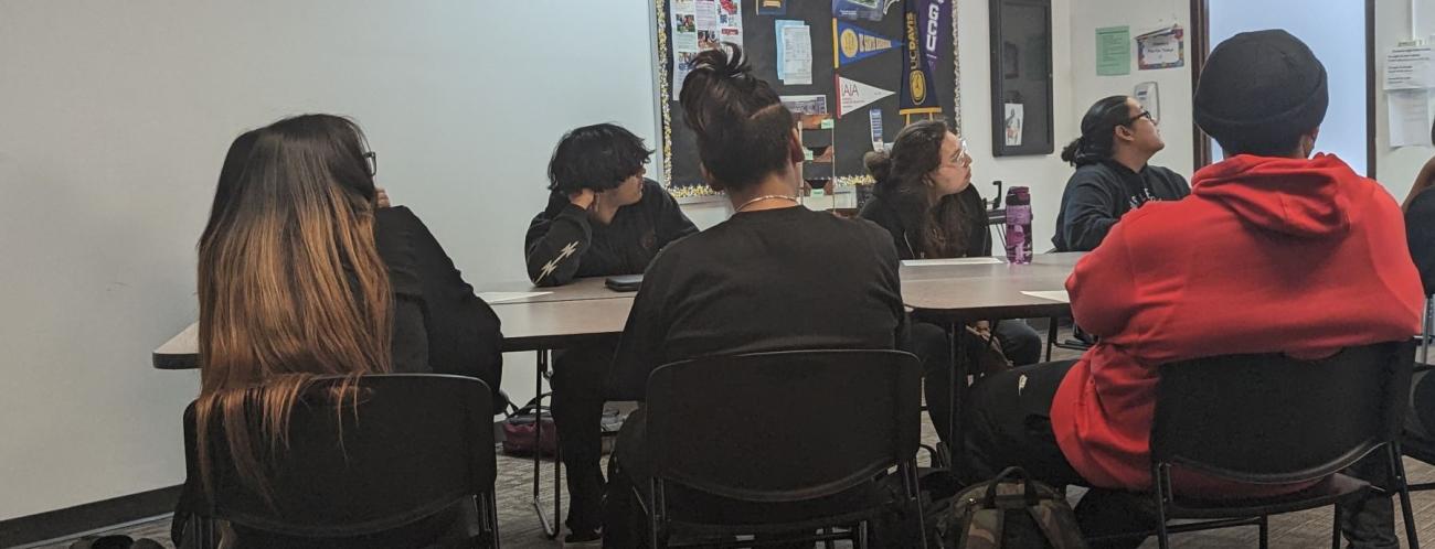 A classroom with students gathered at a table, participating in a group activity or discussion.