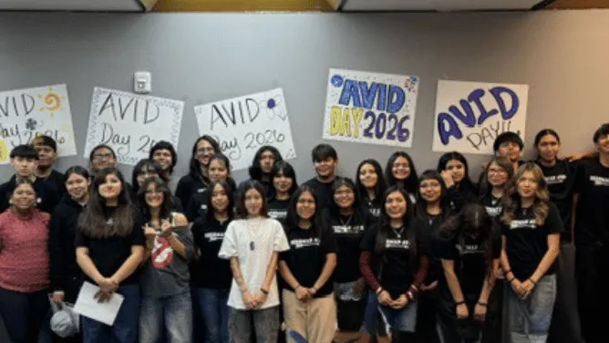 A group of students and staff pose together in front of posters celebrating AVID Day 2026.
